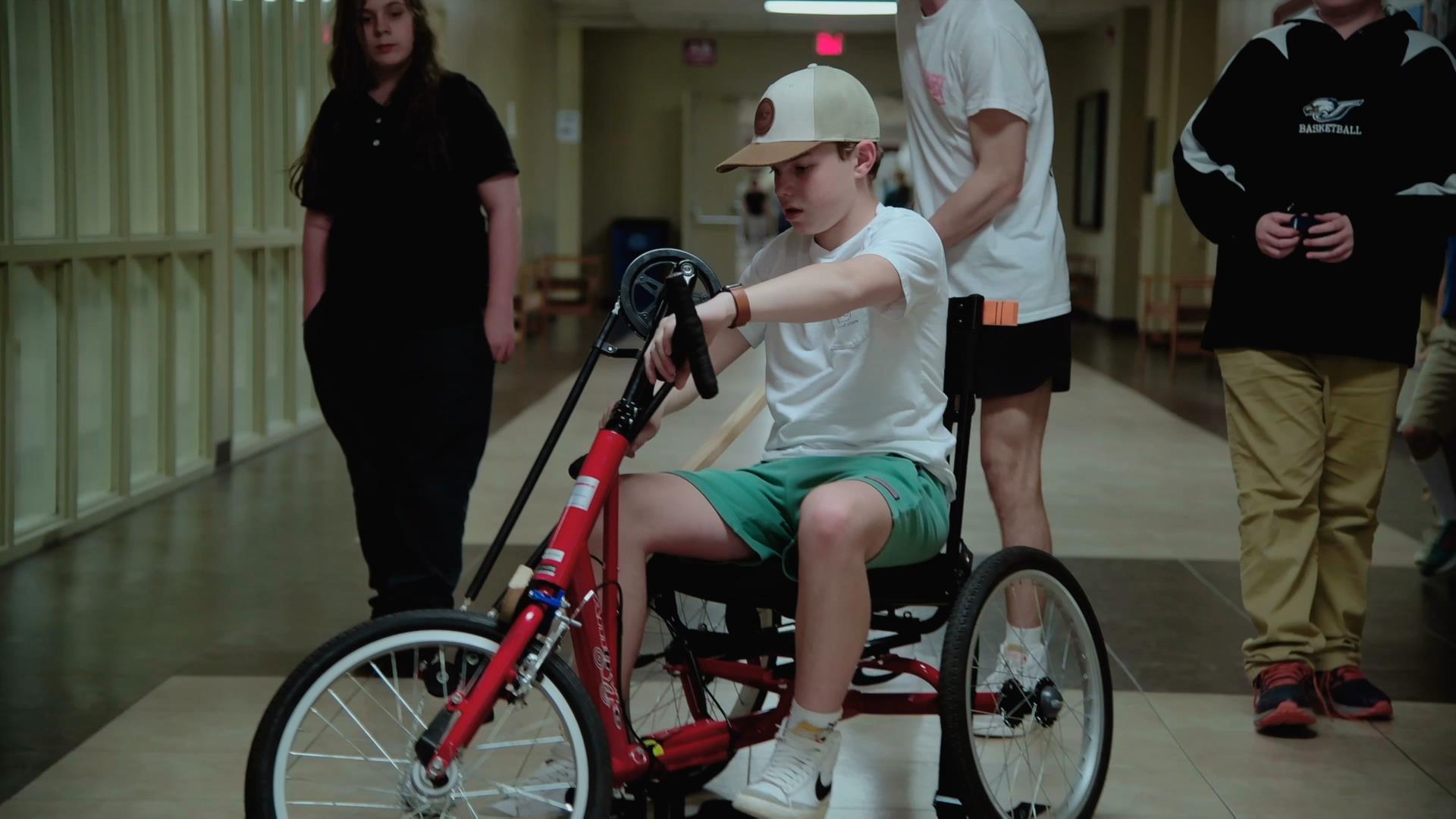 An adapted trike, which utilises a long handle mechanism that allows therapists to steer the trike from behind.