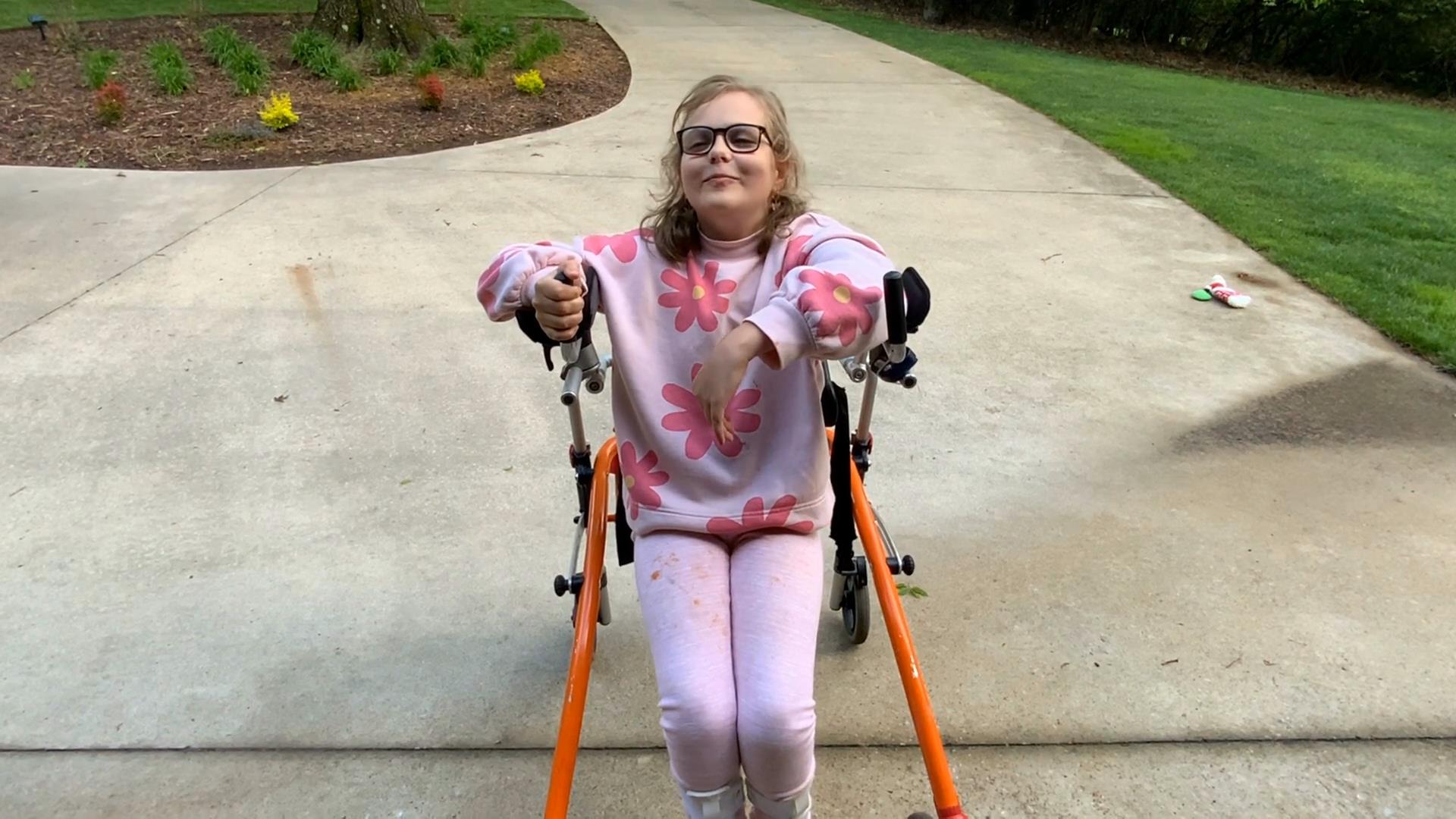 A young students sat in an assistive walker outside.